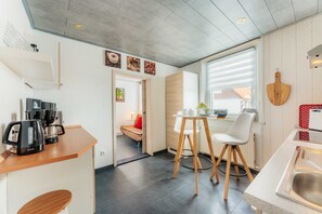 A modern kitchen with a dining area, a coffee machine, and a window with blinds.