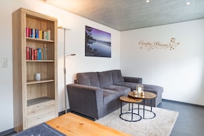 Una sala de estar moderna con un sofá gris, una estantería de madera, una mesita redonda y un cuadro colgado en la pared.