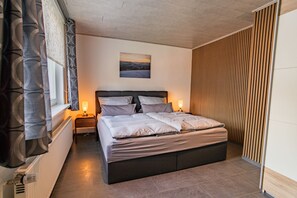 A bedroom with a bed, bedside lamps, a radiator, and a window with curtains.