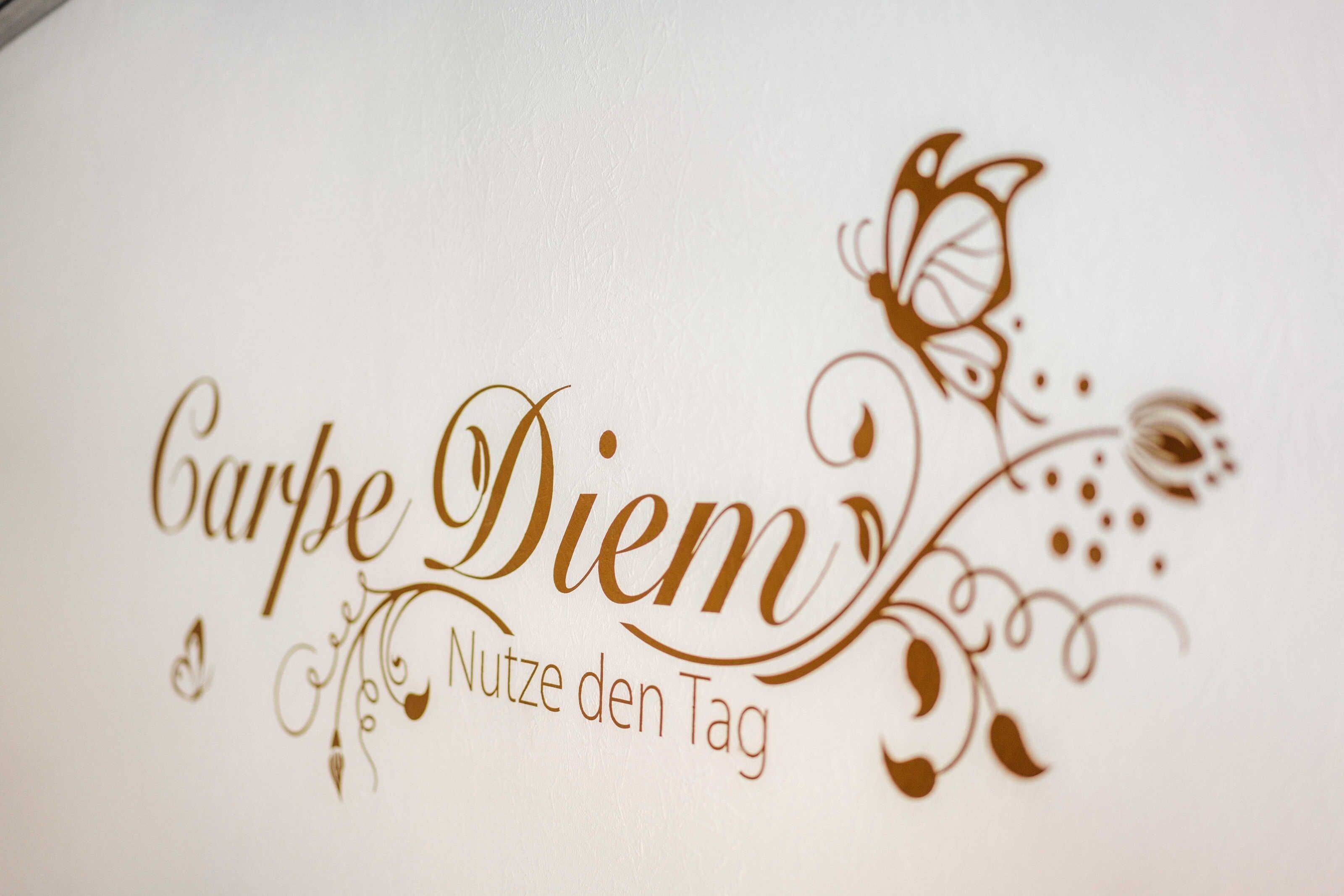 Ein weißes Schild mit der Aufschrift 'Carpe Diem' und 'Nutze den Tag' in einer verzierten Schrift.