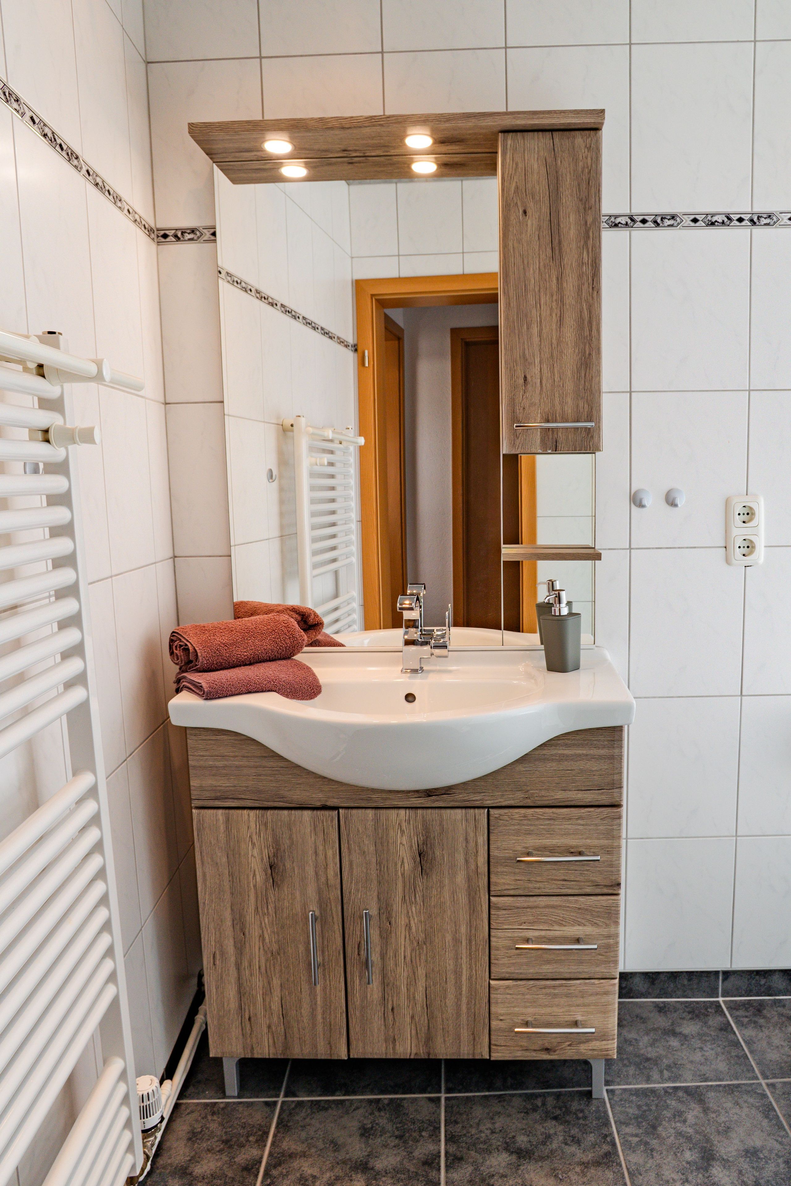 A bathroom with a white sink, wooden cabinets, a mirror, and a towel.