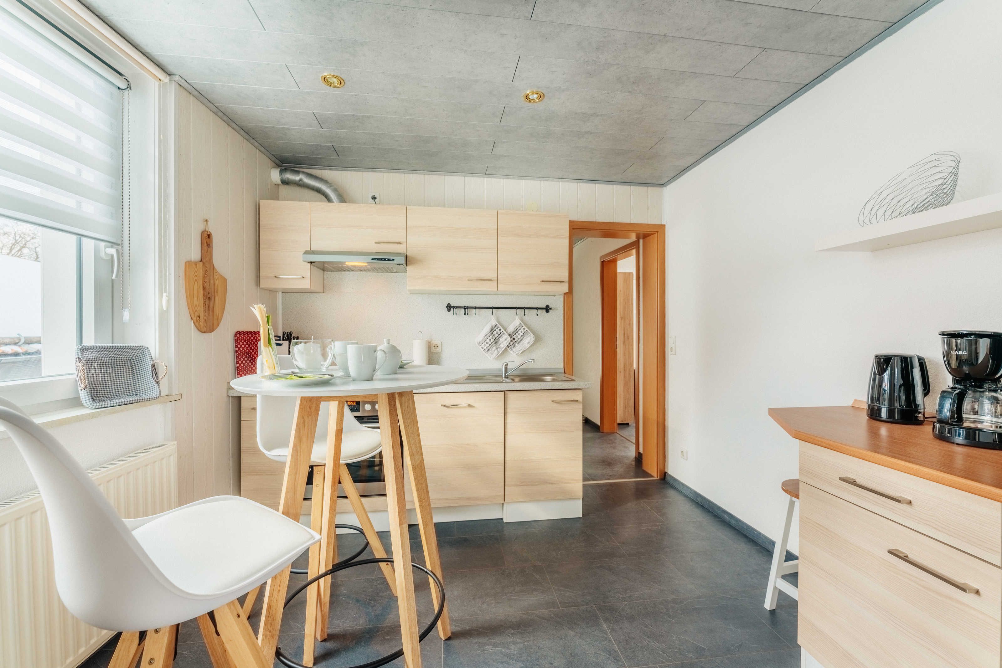 A modern kitchen with wooden cabinets, a white countertop, and a dining area with a white chair.