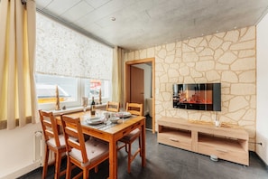 A dining area with a stone wall, a flat-screen TV, and a table set for two.