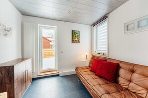 A room with a brown leather sofa, a wooden cabinet, a door leading outside, and a window with blinds.