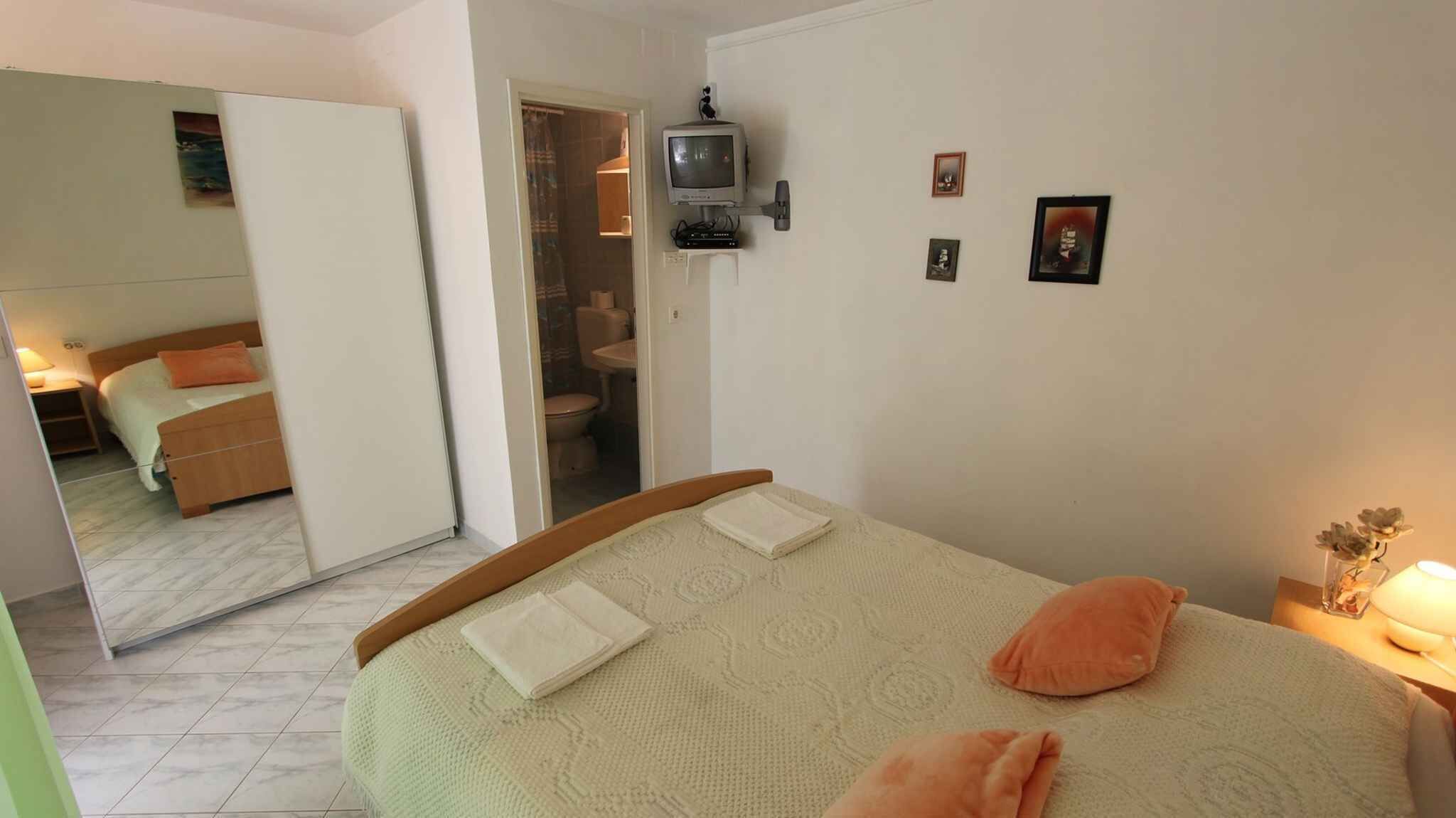Un dormitorio con cama, un espejo, una televisión y una mesita de noche con lámpara.