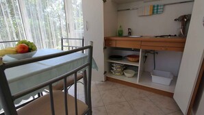 A kitchen with a dining table, chairs, and a fruit bowl. There is a window with a view of greenery. - Studio with air conditioning and terrace (Porat)