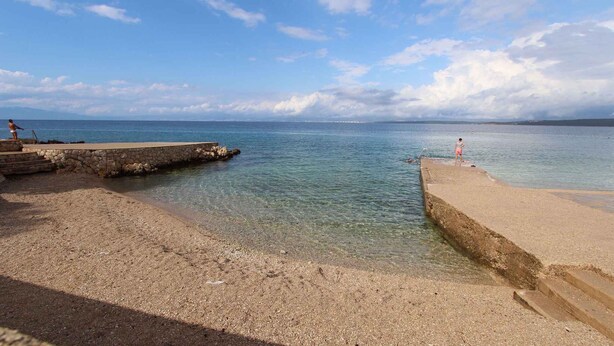 A pebbled beach with clear water, a stone pier, and a distant shoreline. - Studio with air conditioning and terrace (Porat)