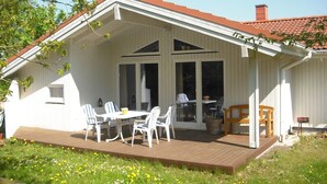 Un edificio bianco con veranda in legno, portico coperto con tavolo e sedie, e un camino.