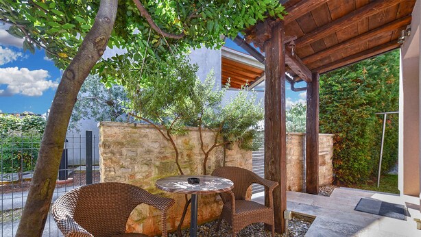 An outdoor seating area with wicker chairs and a round table, surrounded by a stone wall and a wooden pergola. - Holiday apartment mit Klimaanlage und Terrasse (Fa��������ana)