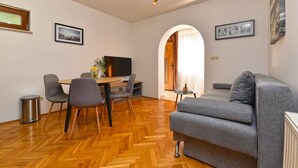A modern living room with a grey sofa, wooden herringbone flooring, a dining area with chairs and a table, a TV, and framed pictures on the walls. - Holiday apartment mit Klimaanlage und Terrasse (Fa��������ana)