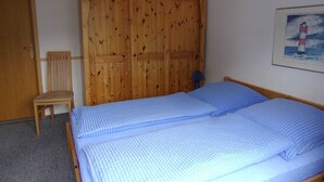 Une chambre avec une armoire en bois, un lit simple avec une literie bleue, une chaise en bois et un tableau encadré représentant un phare, accroché au mur.