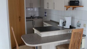 Une cuisine compacte dotée d’un îlot central, de chaises en bois, d’un four encastré et d’un micro-ondes posé sur une étagère.