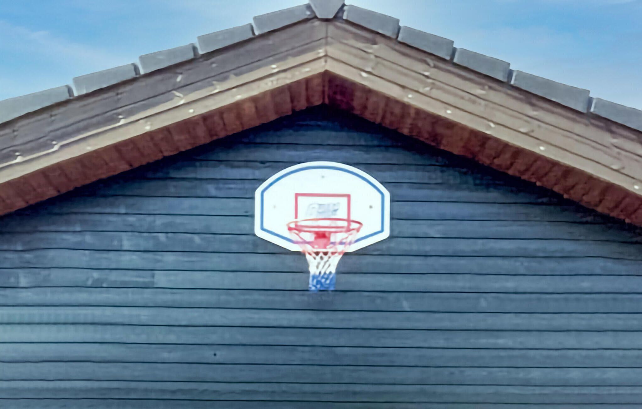 Un panier de basket fixé à un mur en bois, sous un toit en pente.