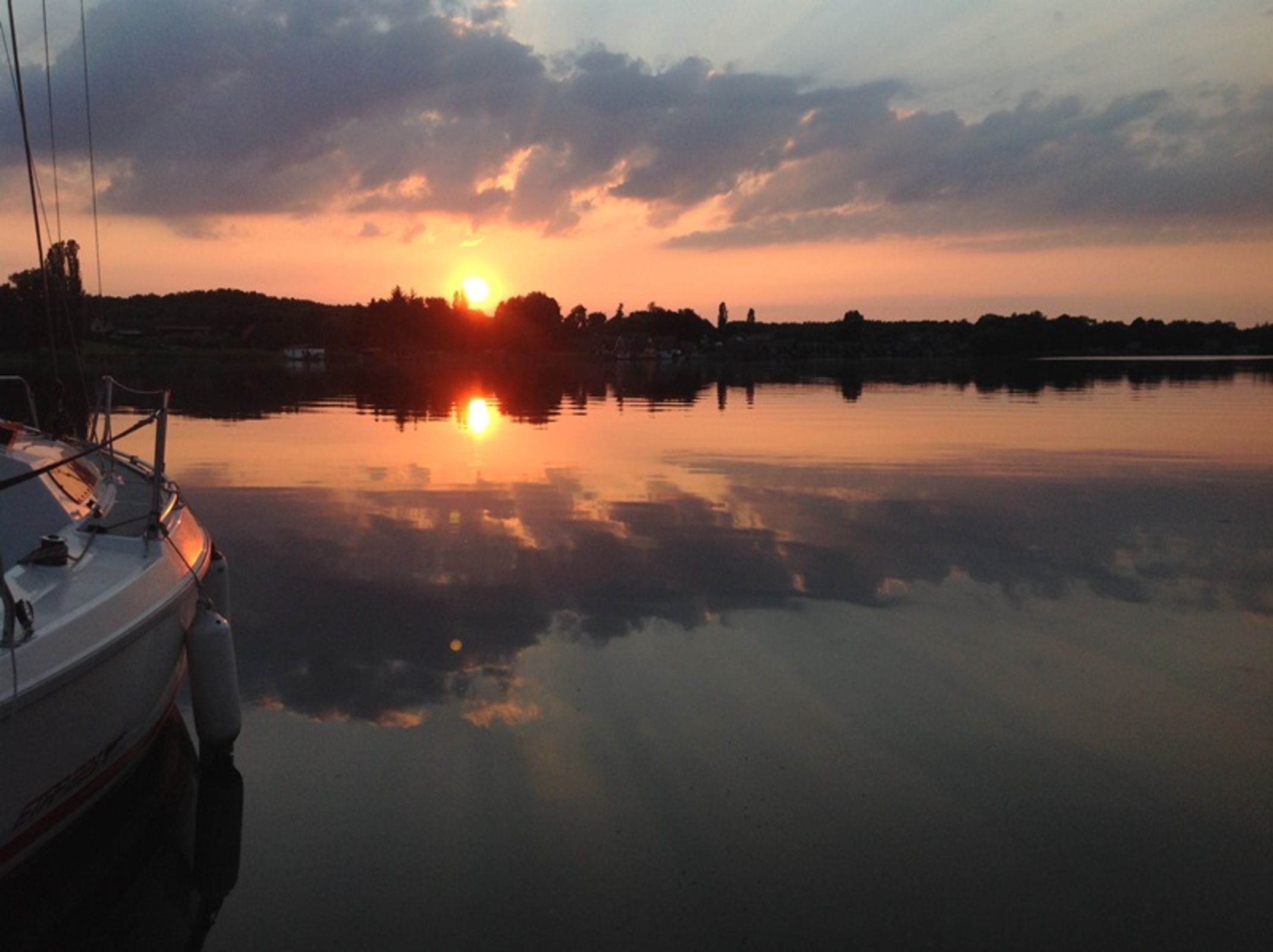 Un lac paisible au coucher du soleil, avec un bateau amarré sur la gauche.