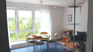 A room with a dining table, chairs, a bookshelf, a sofa, and a view of greenery outside. - Vacation apartment on Lake Mirower See (without balcony) right Whg.3 - Ferienwohnungen am See (Mirow)