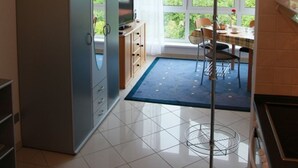 A modern kitchen with a built-in oven, a dining area with a table and chairs, and a large window offering a view of greenery. - Vacation apartment on Lake Mirower See (without balcony) right Whg.3 - Ferienwohnungen am See (Mirow)