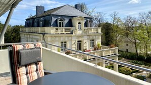 A balcony with a chair and table, overlooking a large building with classical architecture. - Residence Bleichröder- Charlotte, VS Sass - Residence Bleichröder vacation apartment (Heringsdorf)