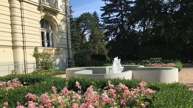 A garden with a fountain, pink flowers, and a building with classical architecture. - Residence Bleichröder- Charlotte, VS Sass - Residence Bleichröder vacation apartment (Heringsdorf)