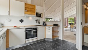 A modern kitchen with white cabinetry, a built-in oven, and a microwave. There is a dining area with a table and chairs visible through an open door. - Beach front home in Rudkøbing with sauna (Rudkøbing)