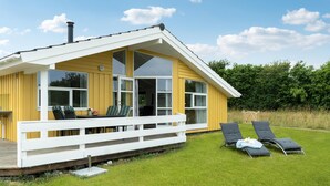 A yellow building with a white porch, large windows, and a deck with lounge chairs. - Beach front home in Rudkøbing with sauna (Rudkøbing)