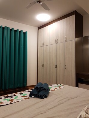 A bedroom with a bed, teal curtains, a wardrobe, and a ceiling fan.