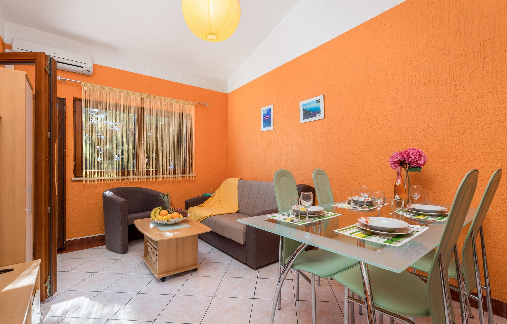 Un coin repas avec une table en verre, des chaises et un canapé. On trouve un panier de fruits sur la table et un vase rempli de fleurs.
