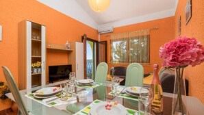 Zona pranzo con tavolo in vetro, sedie e televisore su uno scaffale.