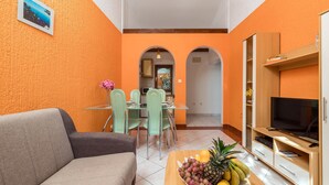 Un ambiente compatto con angolo pranzo, divano, televisore e una ciotola di frutta.