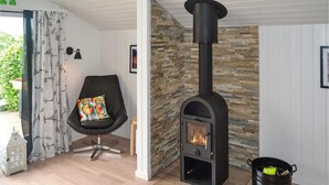 A cozy room with a black wood-burning stove, a black chair with a colorful cushion, and a stone wall. - Nice home in Jægerspris with WiFi (Jægerspris)