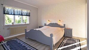 Een slaapkamer met een bed, twee nachtkastjes met lampen, een radiator, een raam met gordijnen en een vloerkleed.