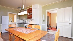 Een kleine keuken met een eethoek, met een houten tafel, stoelen, een koelkast en een fornuis.