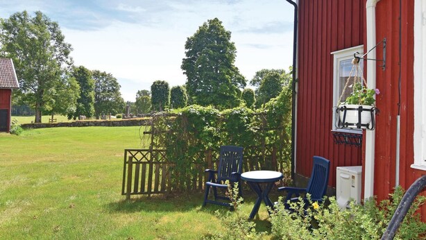 Een rood gebouw met een witte deur, een klein tafeltje, twee blauwe stoelen en een hangende lamp.