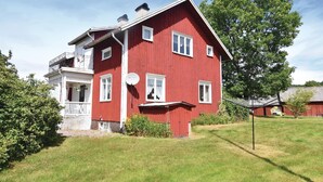 Een rode, twee verdiepingen tellende woning met een balkon, een schotelantenne en een grote boom op de achtergrond.