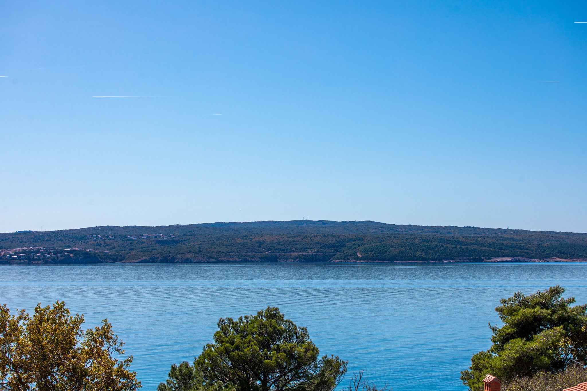 Une vue dégagée sur un lac, avec une colline lointaine et des arbres au premier plan.