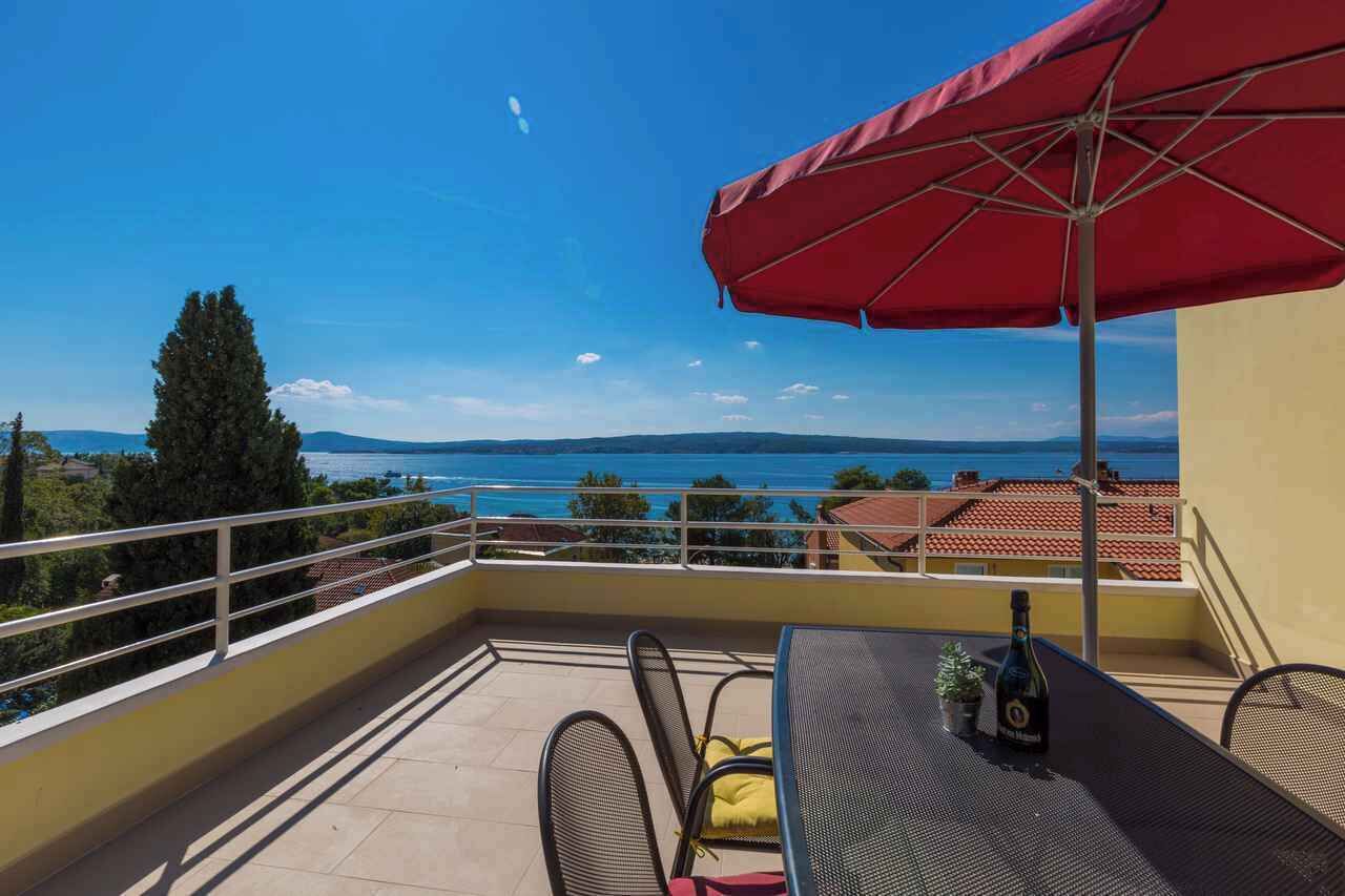 Ein Balkon mit rotem Sonnenschirm, einem Tisch und einer Weinflasche.
