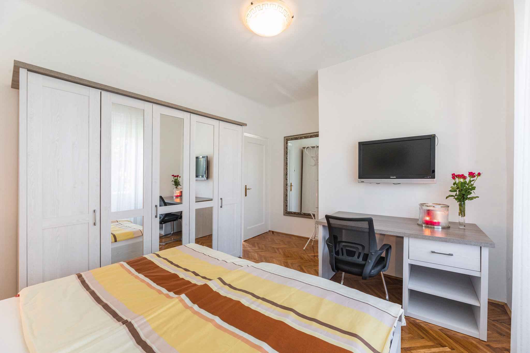 Quarto com cama, escrivaninha, cadeira, televisão e guarda-roupa.