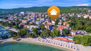 An aerial view of a coastal town with a beach, residential buildings, and a marina.