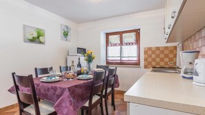 Zona pranzo con tavolo imbandito per quattro, cucina con lavello e macchina del caffè, e finestra con tende.