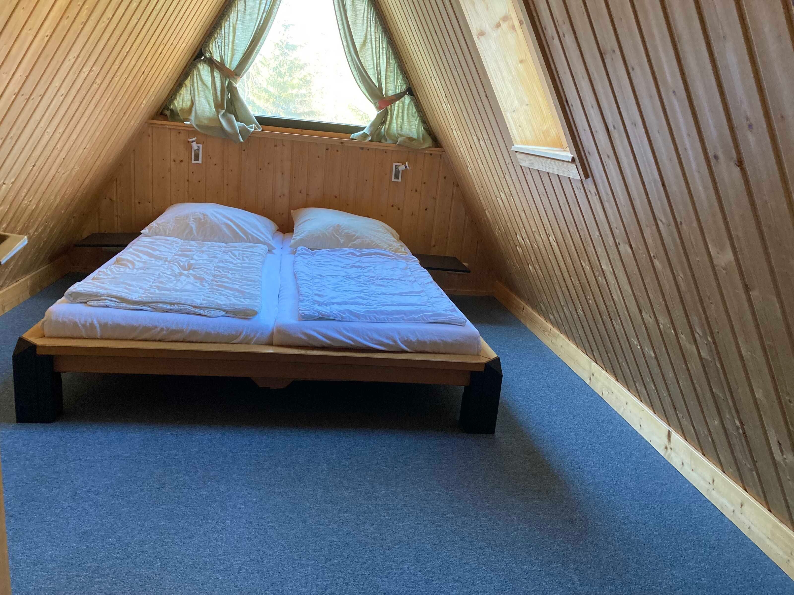 Una cama individual en una habitación de madera con techo inclinado y una ventana con cortinas.
