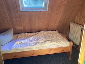 Ein kleines Zimmer mit einem Einzelbett, Holzwänden, einem Oberlicht und einer Heizung.