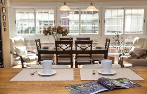A dining area with a wooden table, two white cups on saucers, a magazine, and a view of the city through large windows. - 3 bedroom amazing apartment in Sevilla (Sevilla)