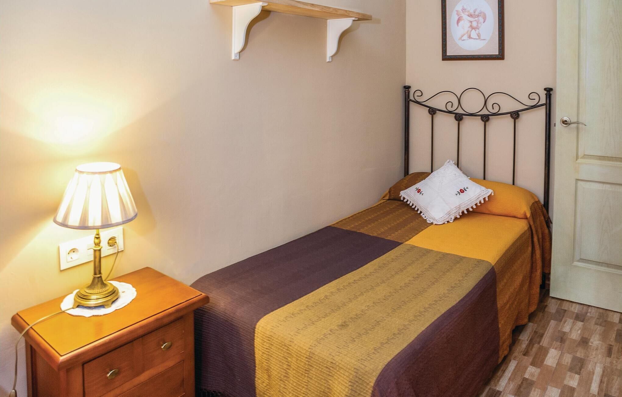 A neatly arranged bedroom with a bed, a bedside table with a lamp, a wall-mounted shelf, and a door.