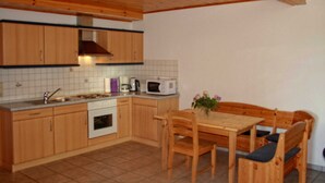 Eine kompakte Küche mit Holzausstattung, einer Mikrowelle, einem Herd und einem Esstisch mit Stühlen.