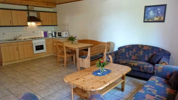 Ein gemütliches Wohnzimmer mit einem Holzesstisch und einem blau gemusterten Sofa.