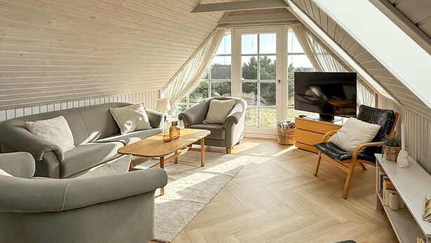 Ein geräumiger Loft-Raum mit hohen Decken, großen Fenstern, einem Fernseher und einer gemütlichen Sitzecke mit einer Couch und Sesseln.