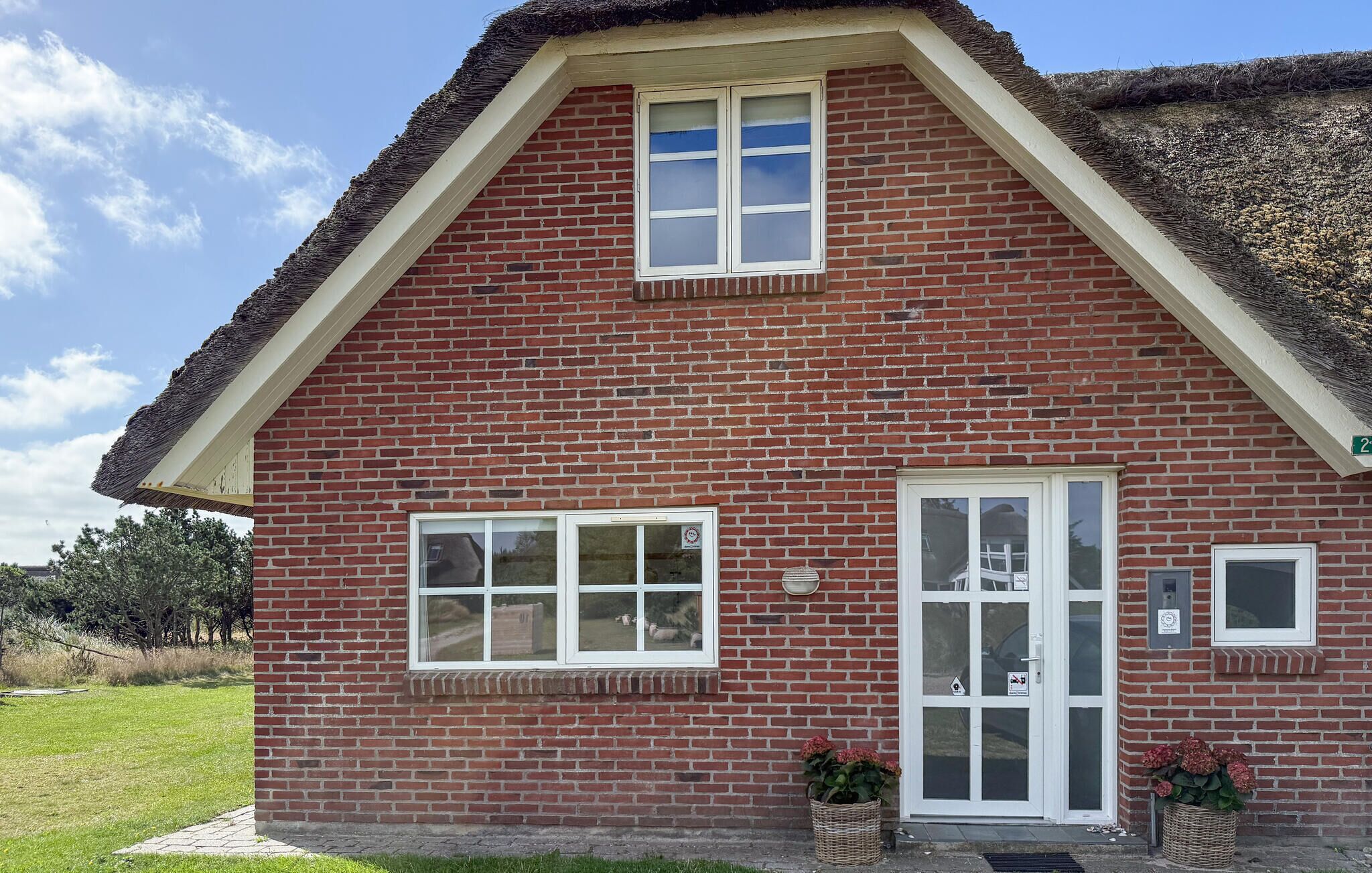 Ein Haus mit roten Ziegelwänden, einem Strohdach und Fenstern mit weißen Rahmen sowie einer Tür mit einer Glasverkleidung.
