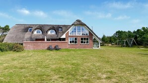 Ein zweistöckiges Haus mit einem Strohdach, einer Ziegelsteinfassade und großen Fenstern.