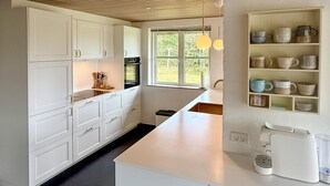 Eine moderne Küche mit weißen Schränken, einem großen Fenster und einer eingebauten Ablagefläche mit verschiedenen Küchenutensilien.