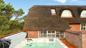 Ein Haus mit einem Strohdach, einem Whirlpool und einer Ziegelaußenwand.