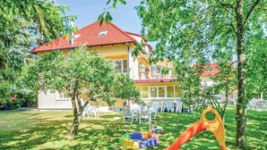A two-story building with a red-tiled roof, surrounded by trees and a grassy lawn. - 4 bedroom cozy home in Grzybowo (Grzybowo)